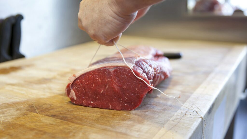 Close up of butchers hands tying meat joint in butchers shop