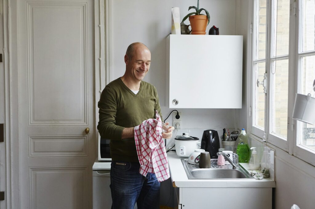 Mature man drying glass at kitchen sink