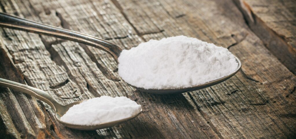 Tablespoon and teaspoon with baking soda, on wooden background. Close up view.