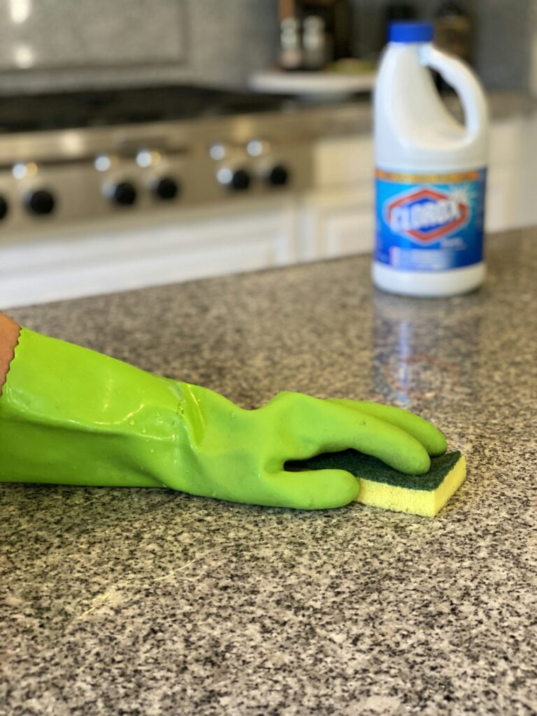 Using rubber gloves and a sponge to disinfect the counters with a bleach solution.