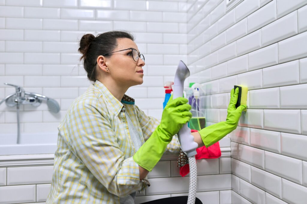 Woman doing bathroom cleaning, washing tile wall with steam