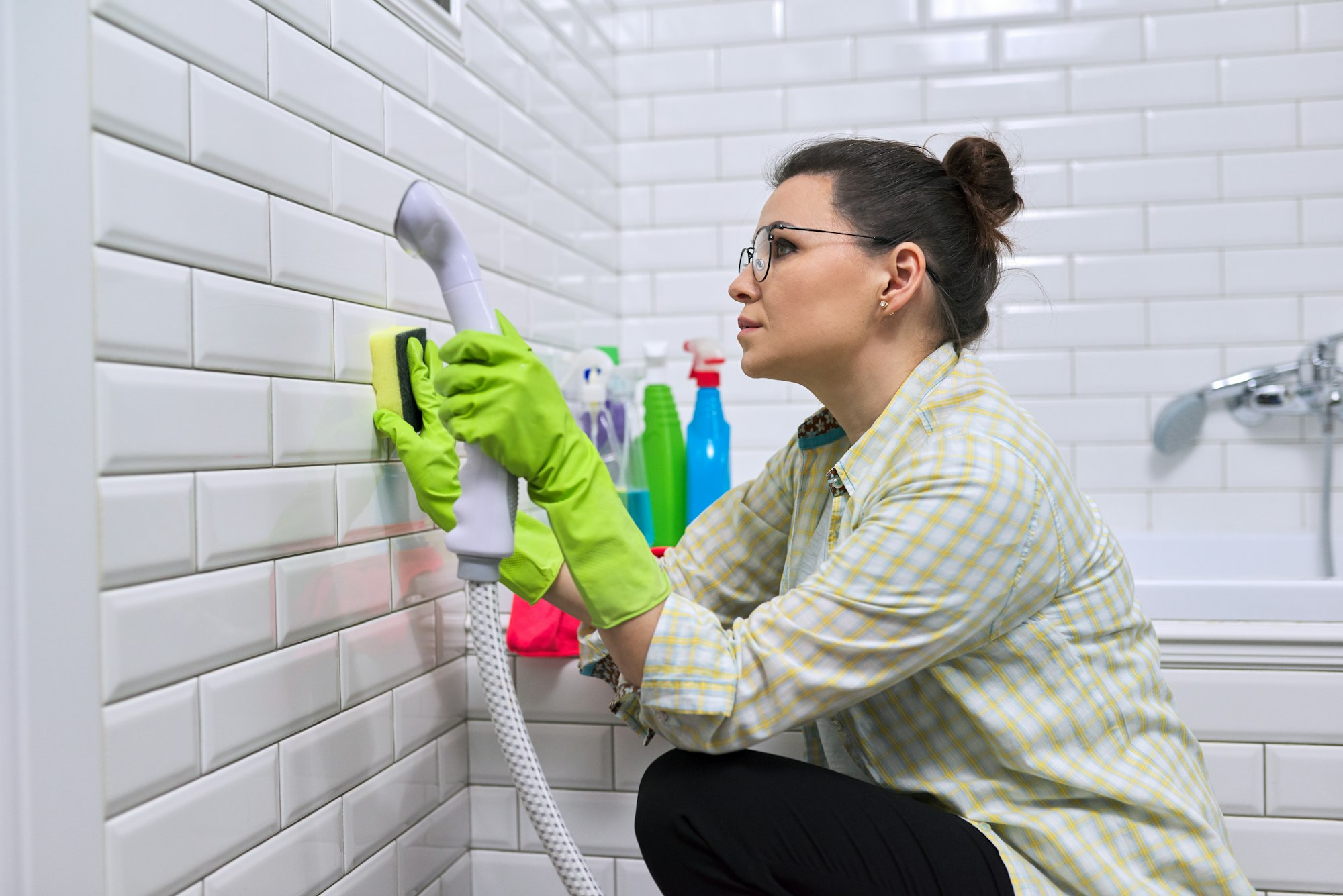 Woman doing bathroom cleaning, washing tile wall with steam