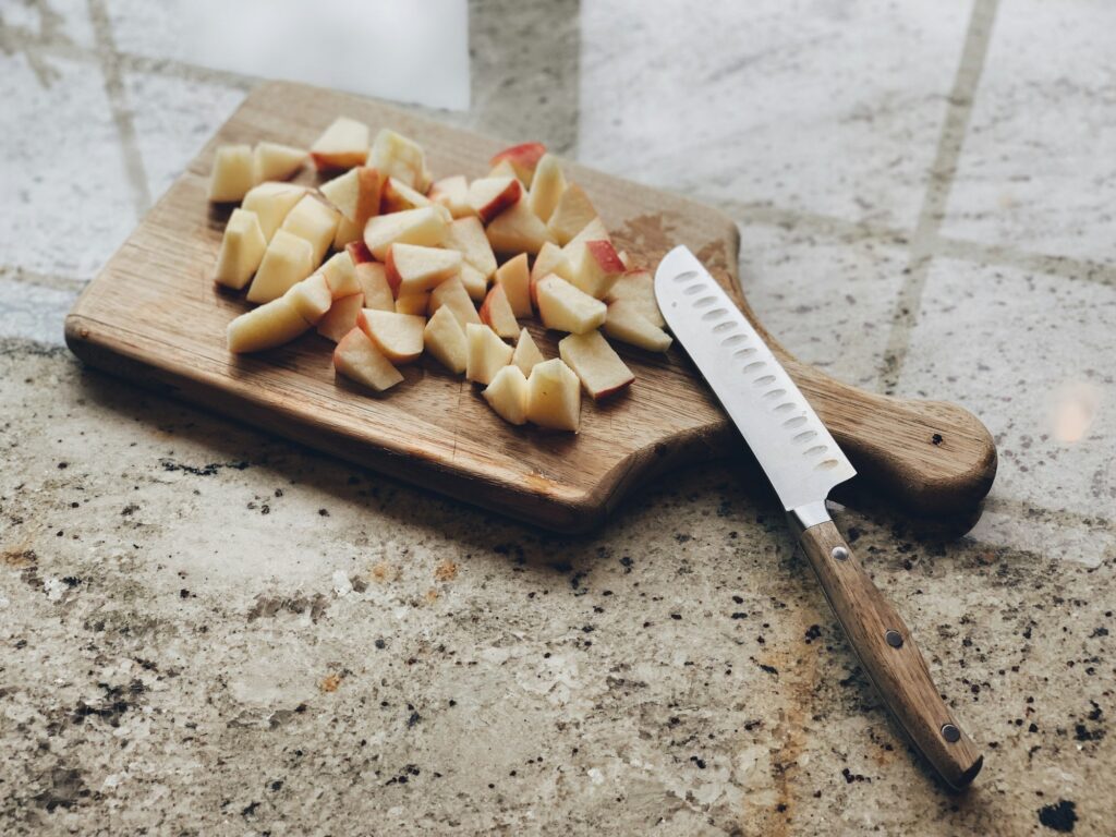 Wooden chopping board with apple wedges and a knife on a granite countertop