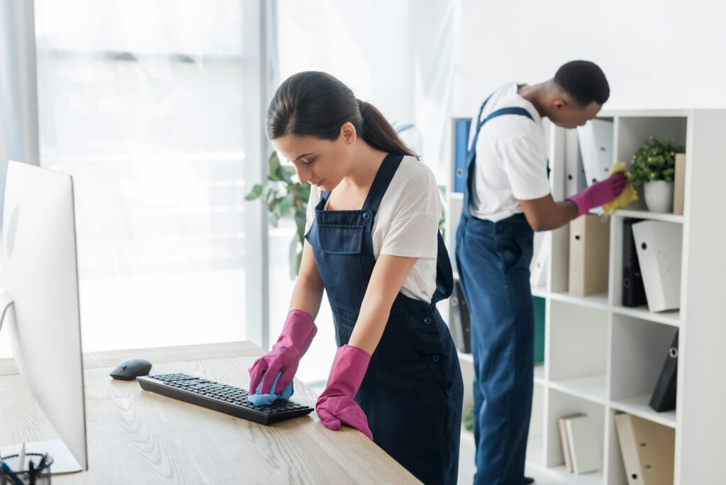 Selective focus of worker of cleaning service cleaning computer keyboard near African american