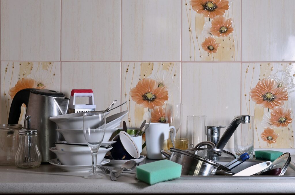 A huge pile of unwashed dishes in the kitchen sink and on the countertop