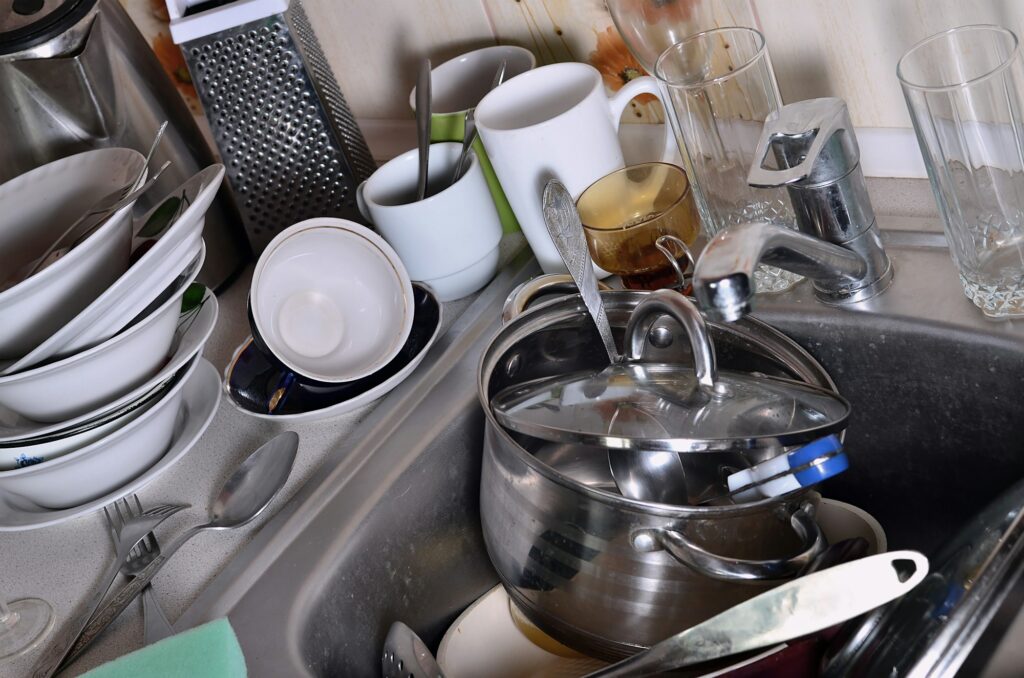 A huge pile of unwashed dishes in the kitchen sink and on the countertop