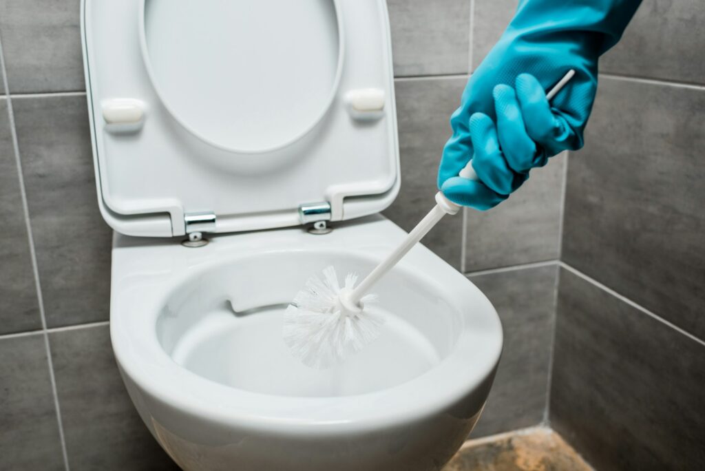 cropped view of cleaner cleaning ceramic toilet bowl with toilet brush in modern restroom with grey