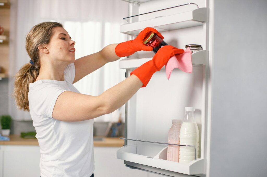 Woman in red gloves is doing cleaning and wash a refrigerator inside